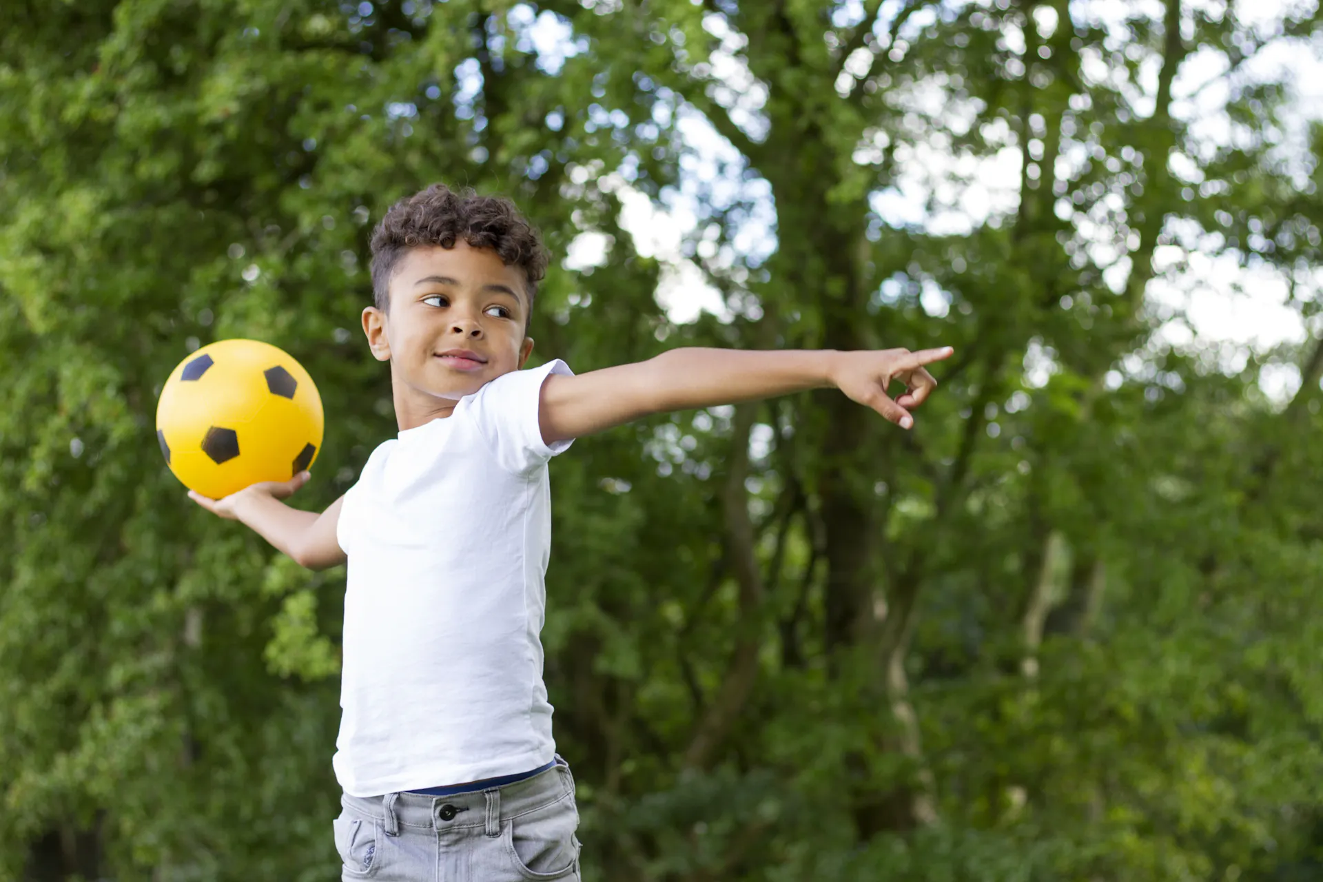 A child holds a soccer ball behind his head, ready to throw, while pointing forward with his other hand.