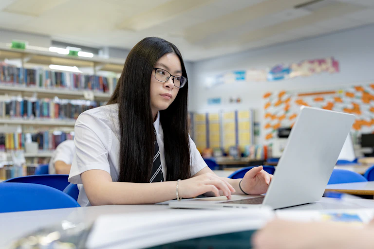 Female high school student studying on a laptop in the school library.
