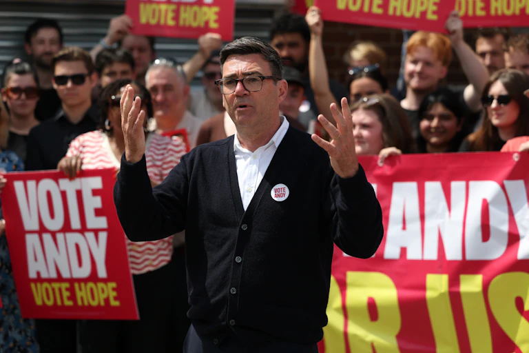 andy burnham campaigning on byelection day in front of crowds holding banners saying vote andy vote hope