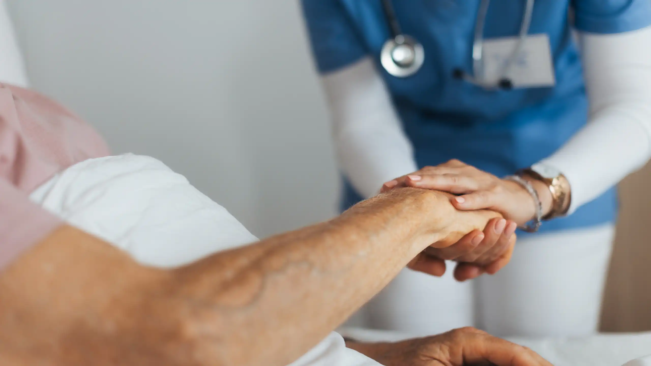 Closeup of a patient's arm, with medical care worker holding their hand