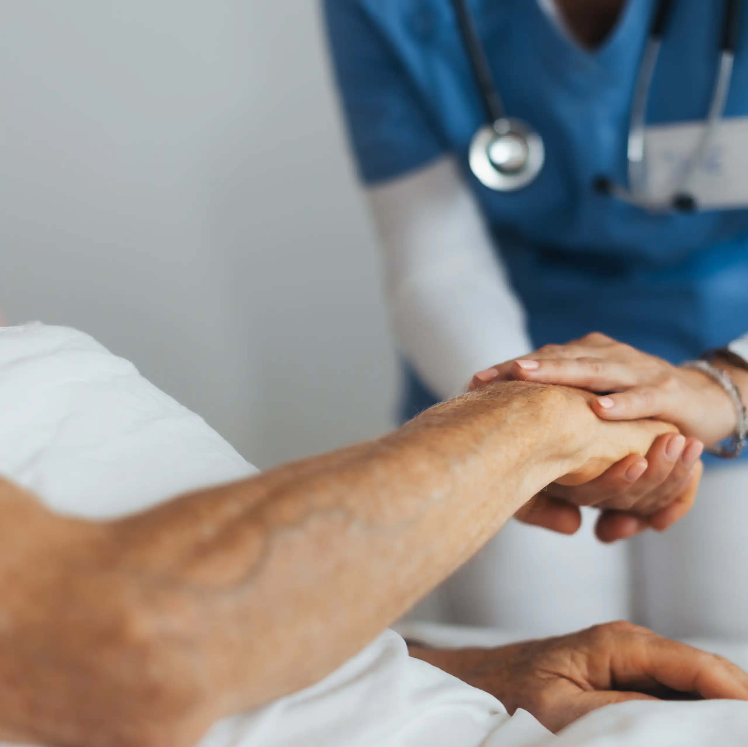 Closeup of a patient's arm, with medical care worker holding their hand