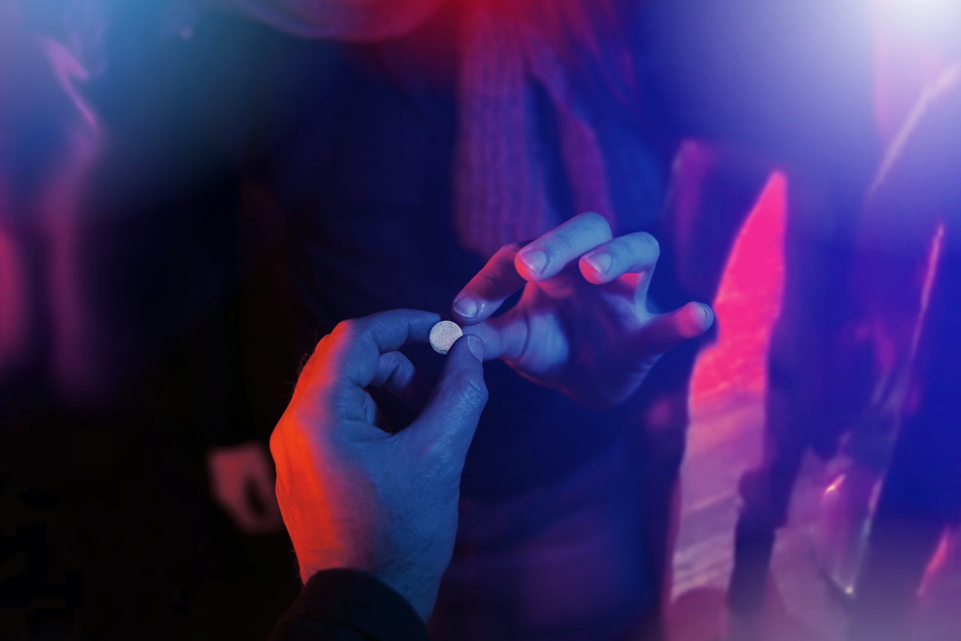 Una mano pasa una pastilla a otra en un ambiente con luces de color.