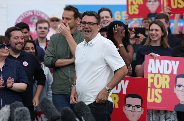andy burnham with supporters holding placards reading andy for us.
