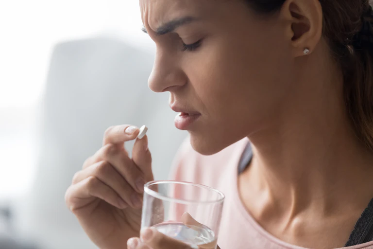 A teen girl holds a pill in one hand and a glass of water in the other.