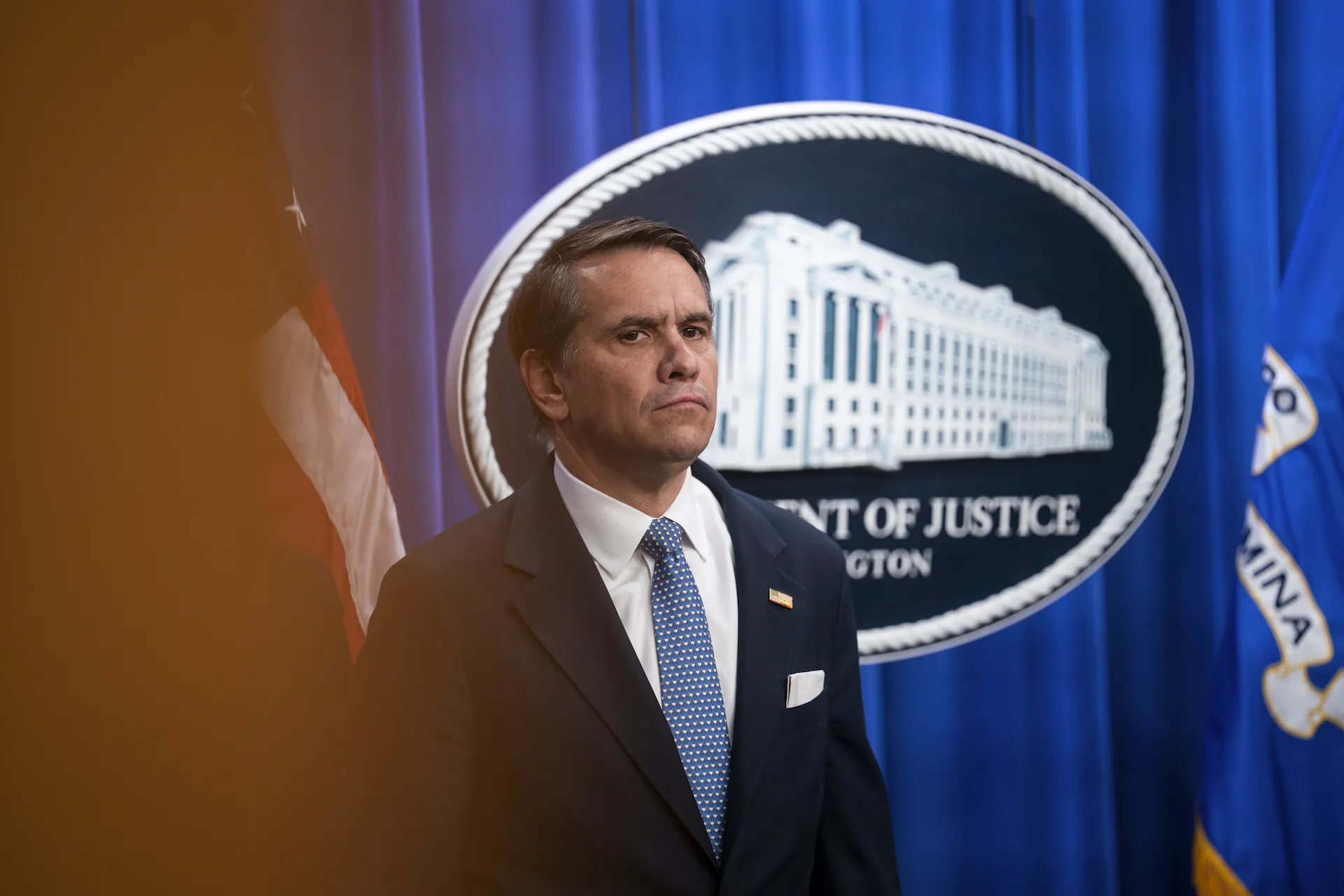 A man in a suit and tie stands on a stage, listening.