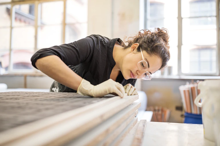 A woman bends over in a carpenter's workshop to examine a join