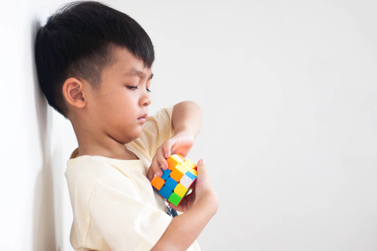 Boy playing Rubik's Cube against a white background.
