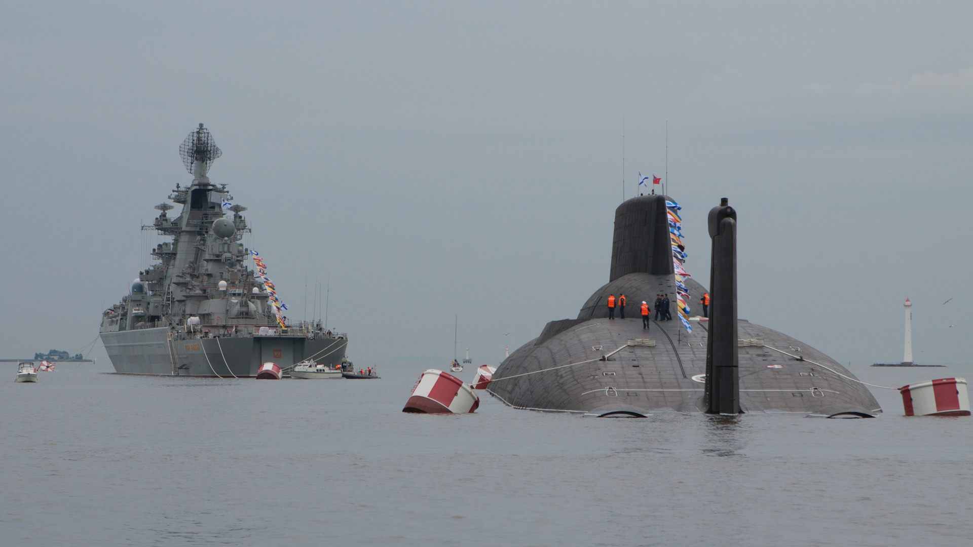 A Russian nuclear submarine surfaces alongside a Russian Navy warship.