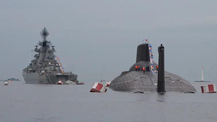 A Russian nuclear submarine surfaces alongside a Russian Navy warship.