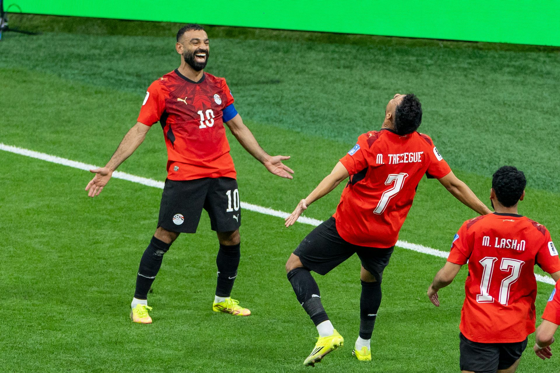 Two men in red jersey smile and celebrate on a soccer field.