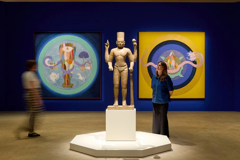 Gallery interior: a woman looks at an ancient statue, modern paintings behind.