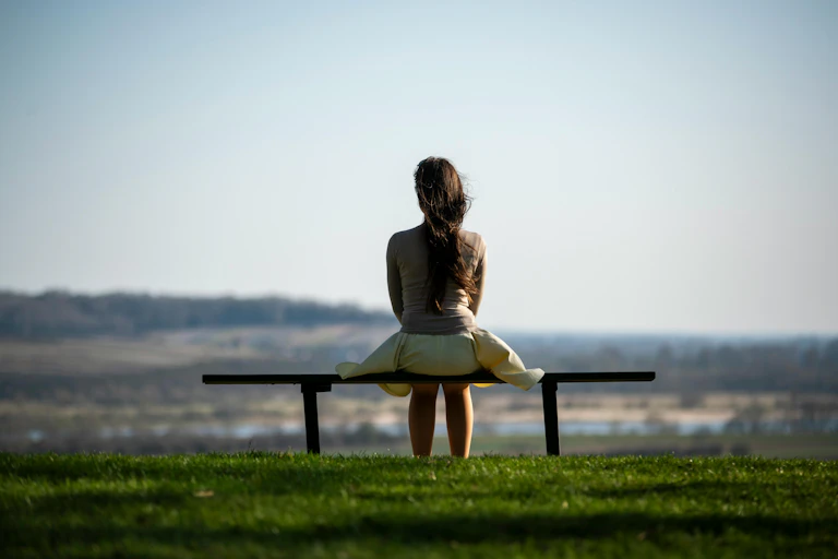 Une femme, vue de dos, assise seule sur un banc.