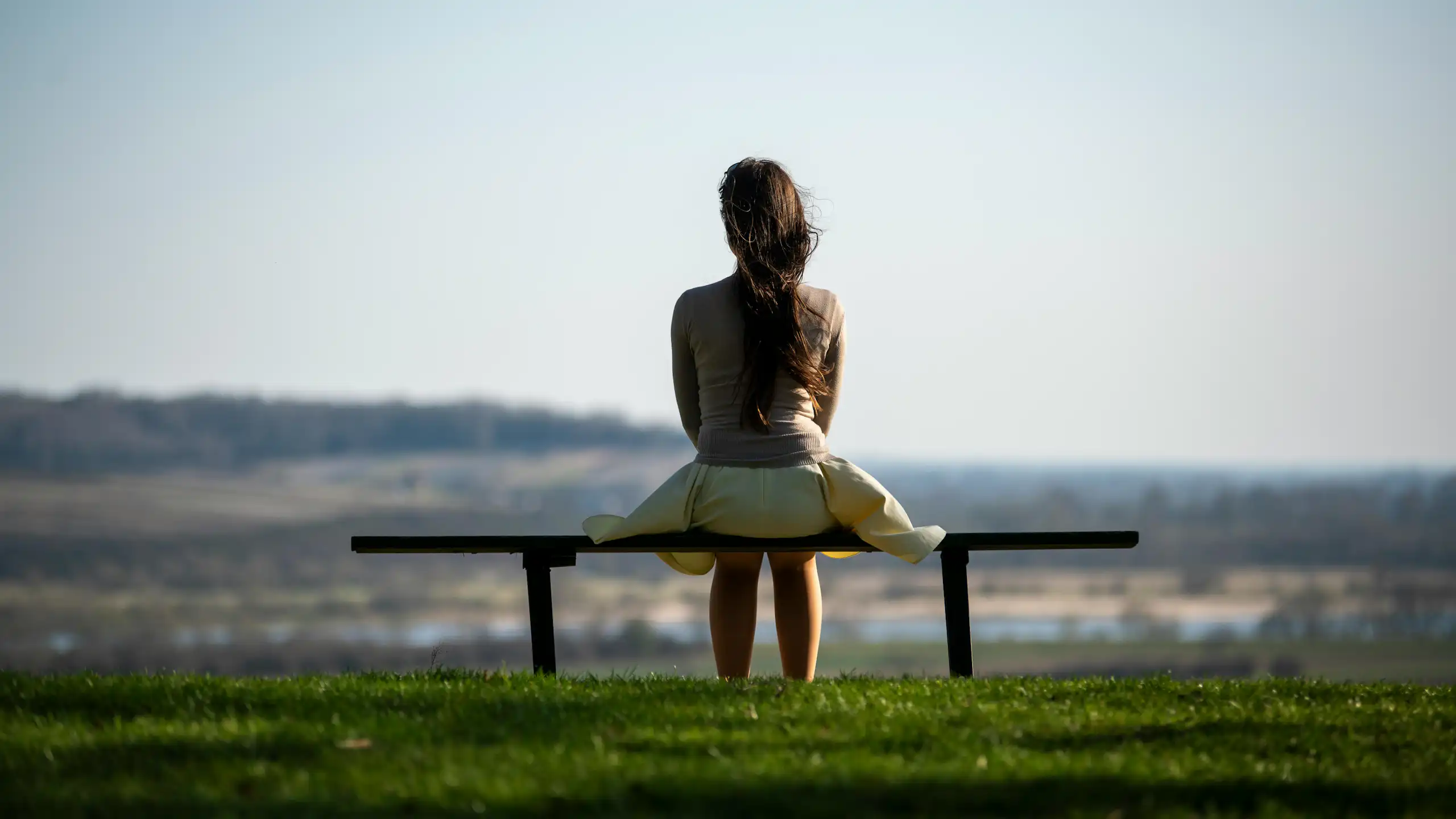 Une femme, vue de dos, assise seule sur un banc.