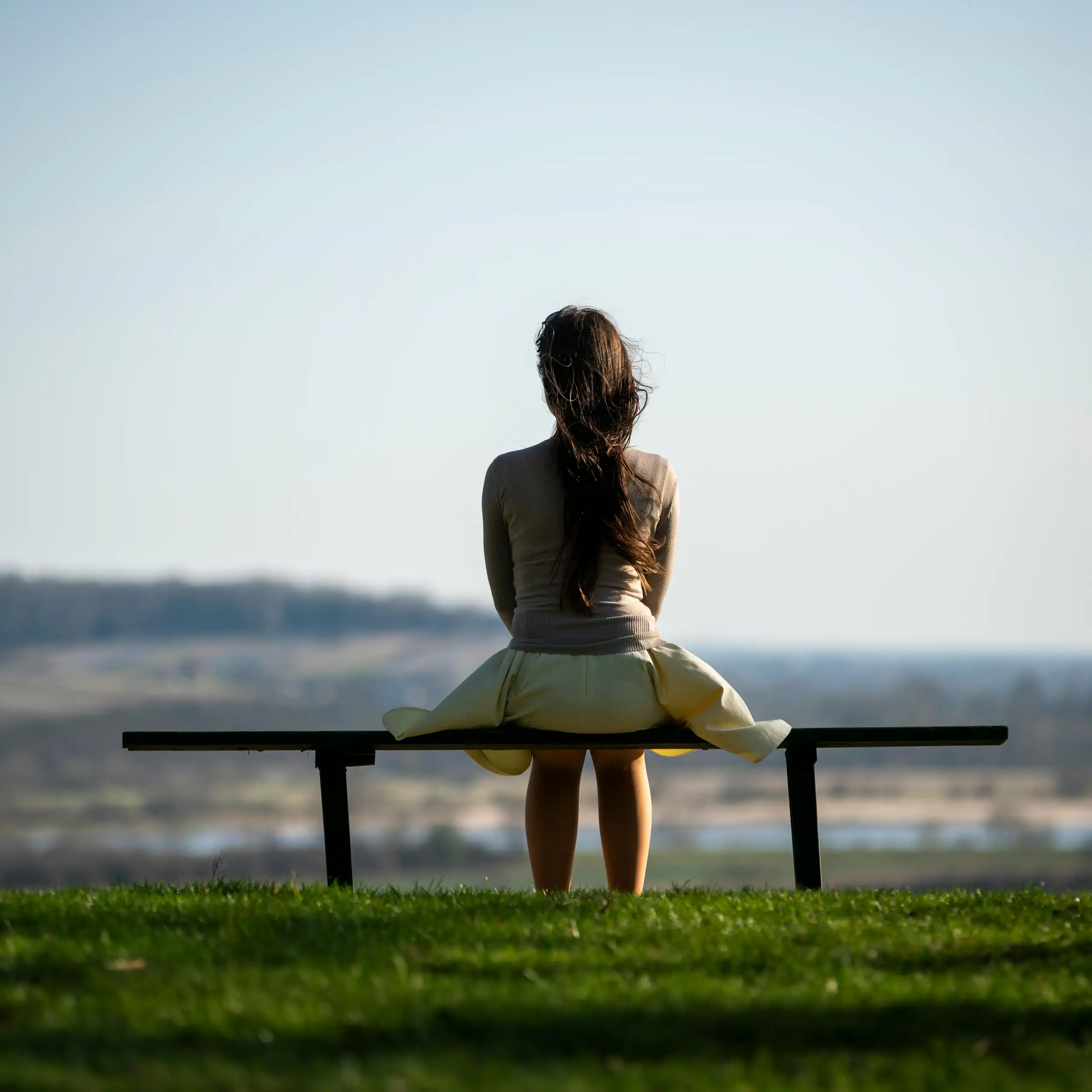 Une femme, vue de dos, assise seule sur un banc.