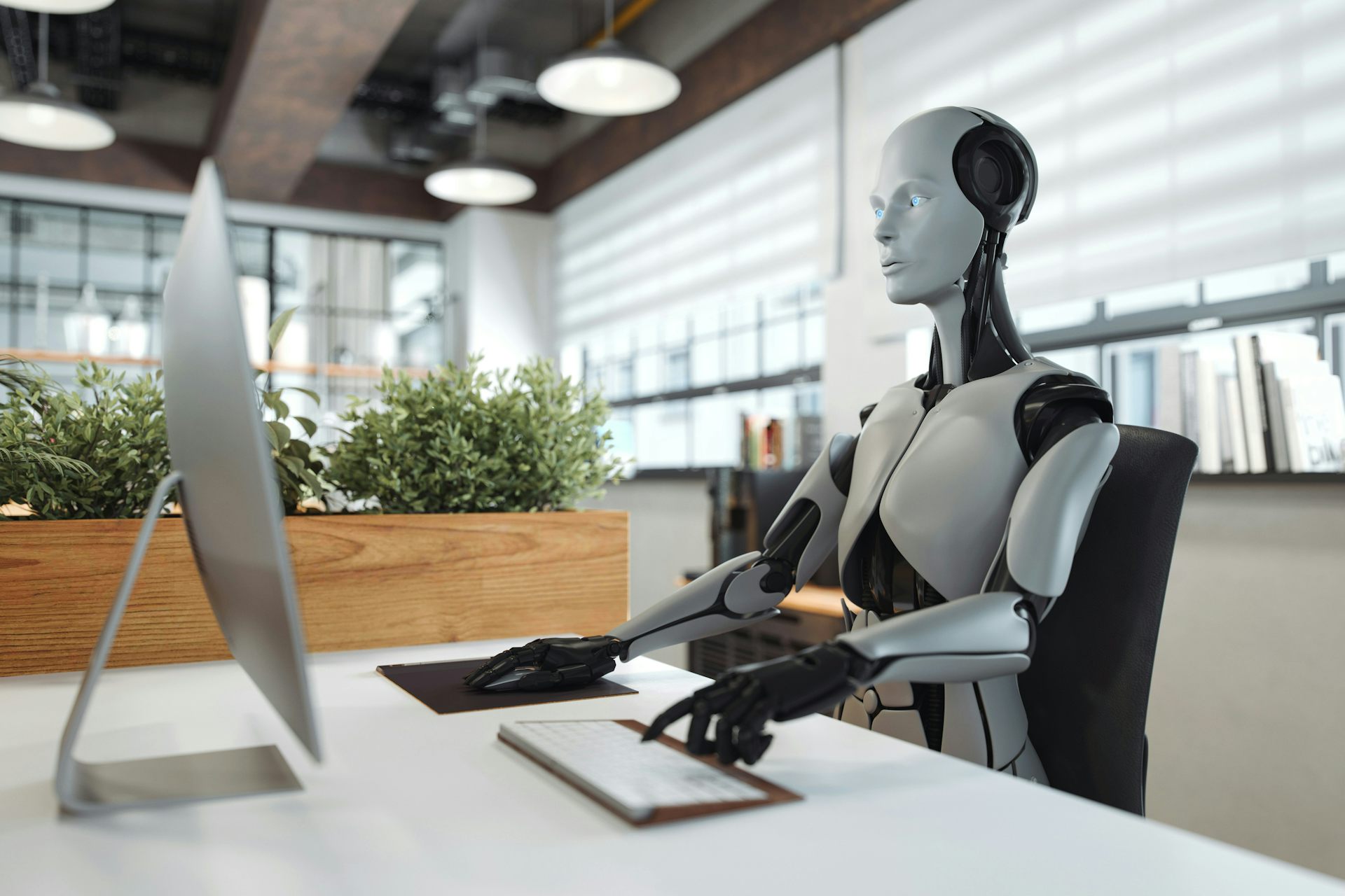 un robot assis à un bureau et tapant sur un clavier en regardant l'écran d'un ordinateur.