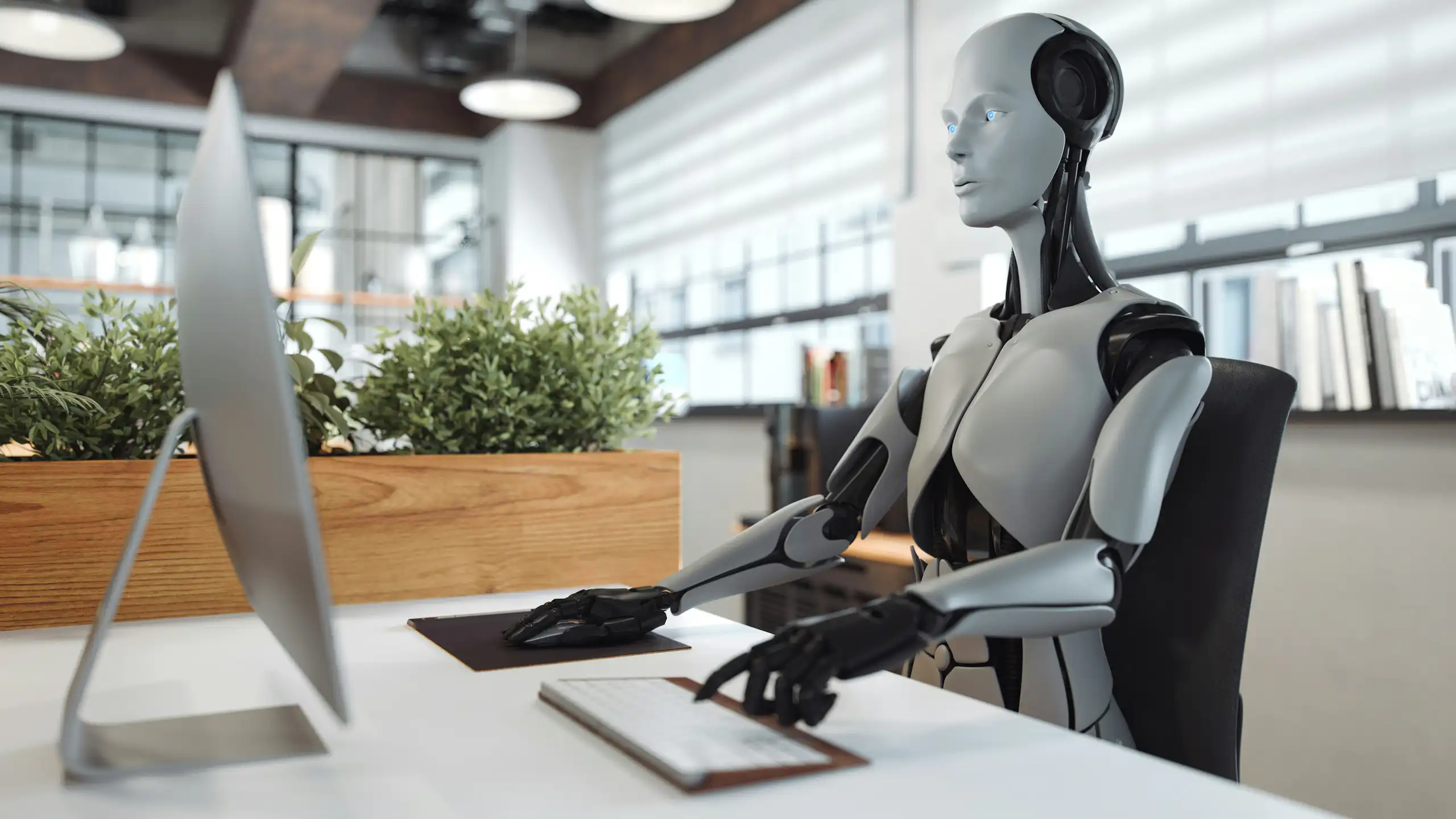 un robot assis à un bureau et tapant sur un clavier en regardant l'écran d'un ordinateur.