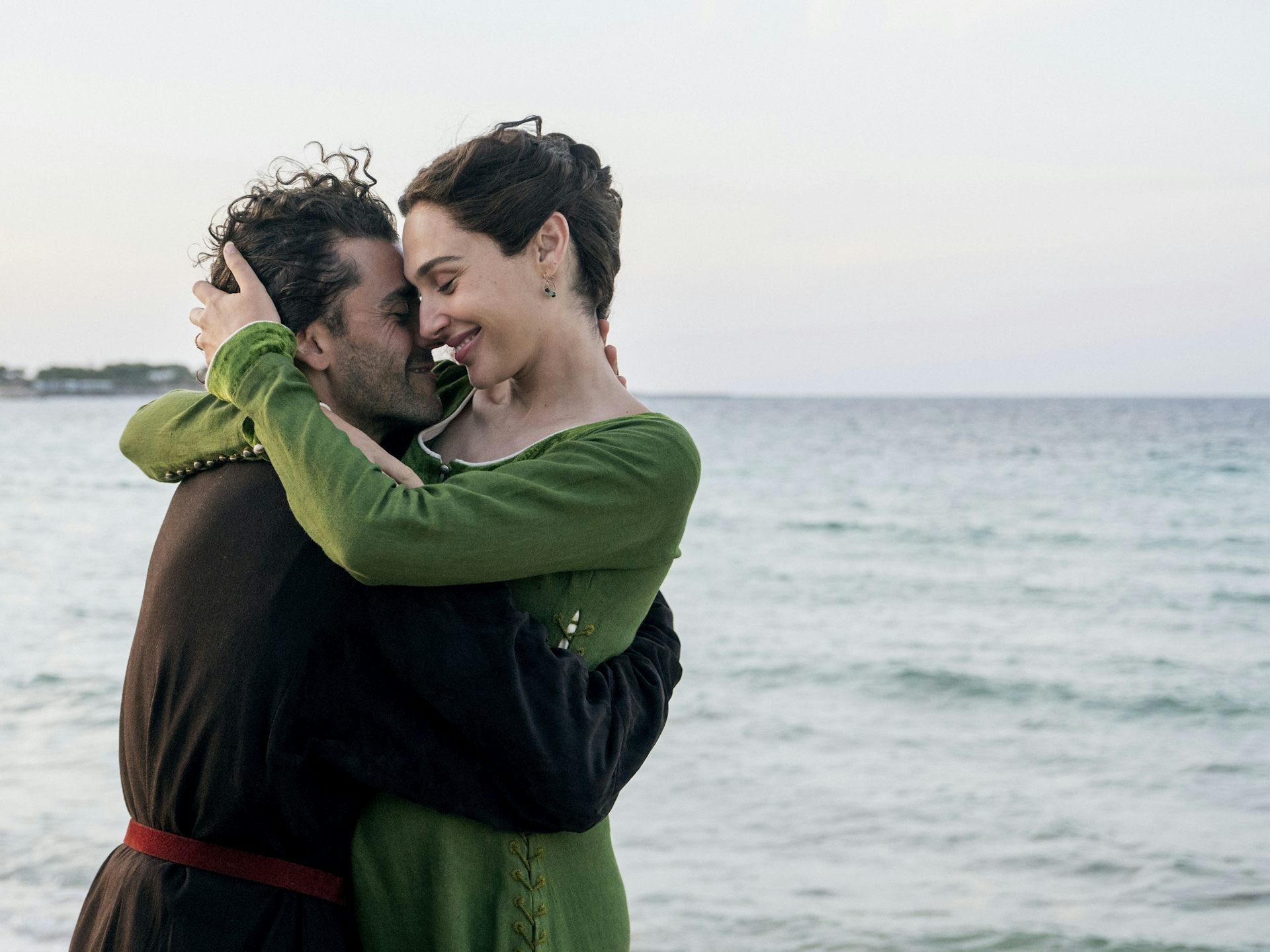 A couple in medieval dress embracing looking happy by the sea.