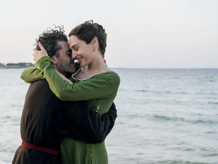 A couple in medieval dress embracing looking happy by the sea.