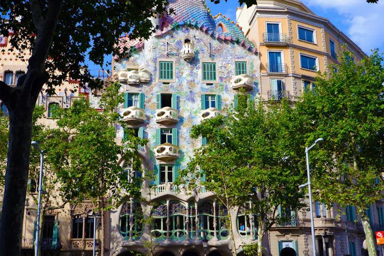 La herencia islámica incrustada en los diseños más famosos de Gaudí 1 Foto de un edificio residencial en el centro de Barcelona, con azulejos de colores y árboles delante.