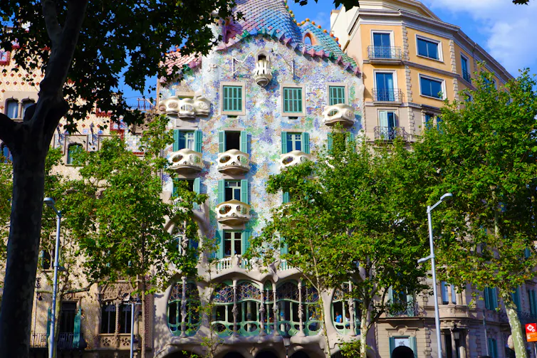 A photo of an apartment building in central Barcelona, with multi-coloured tiles and trees in front.
