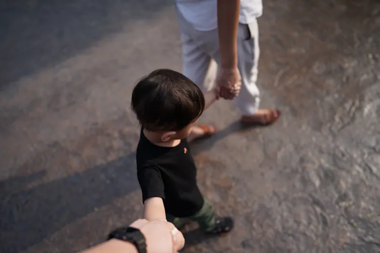 View from above of an anonymous child holding the hands of two adults