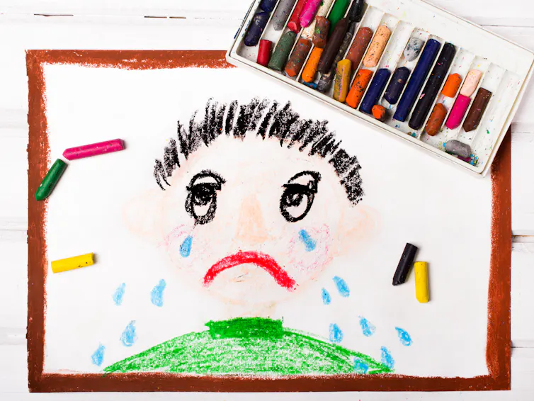 A drawing shows a young child with tears down his face, with a box of crayons nearby.