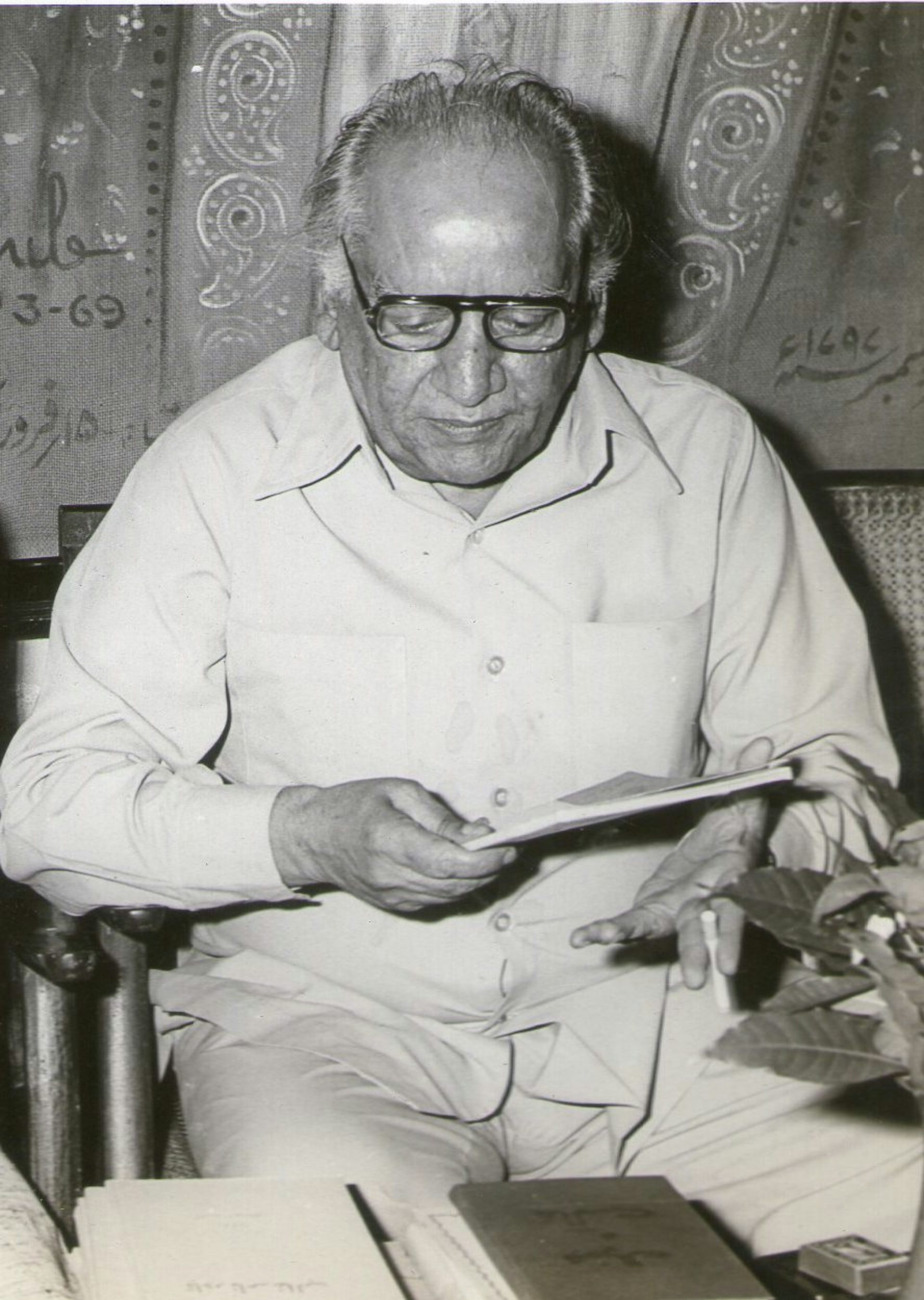 Black-and-white photo of a balding, portly man who's seated, wearing glasses, and glancing down at a notebook.