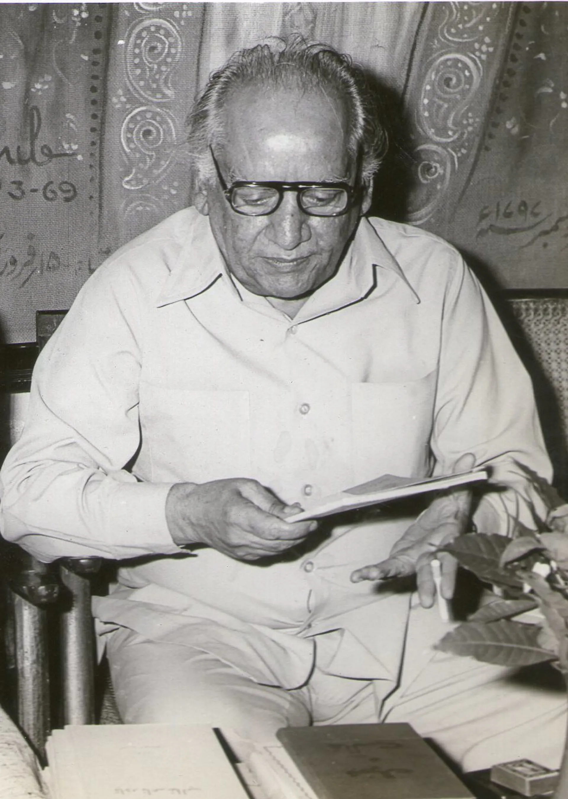 Black-and-white photo of a balding, portly man who's seated, wearing glasses, and glancing down at a notebook.