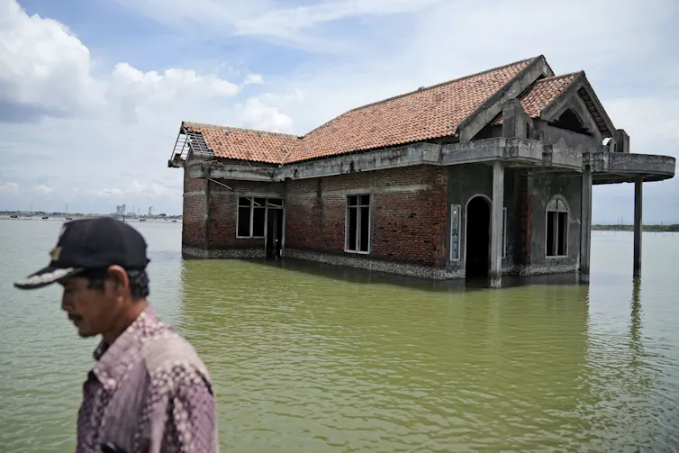 a man walks past an abandoned house surrounded by floodwaters