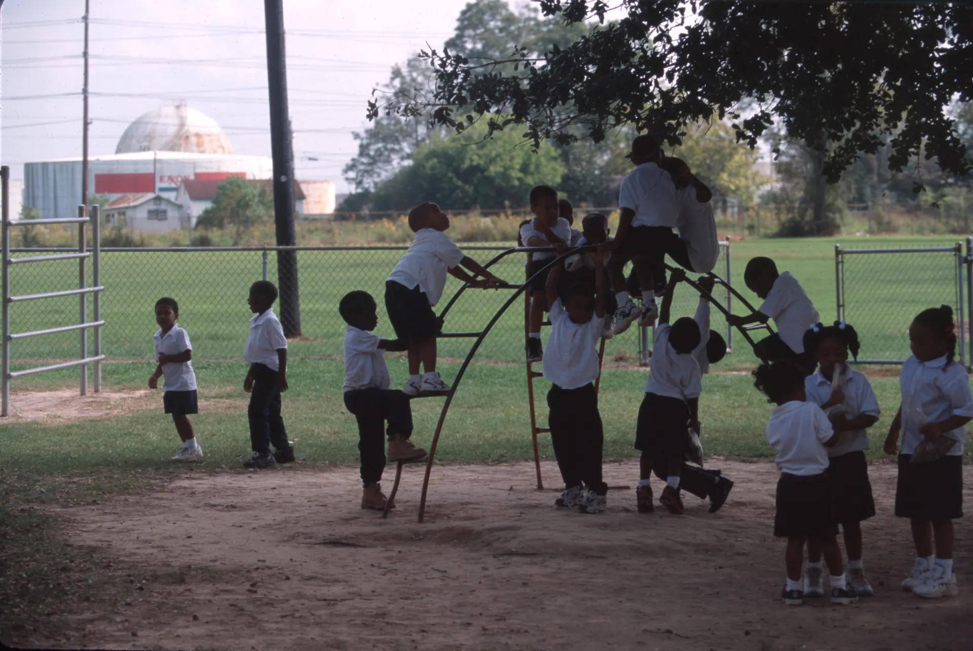Children play on a playground with an industrial building in the background.