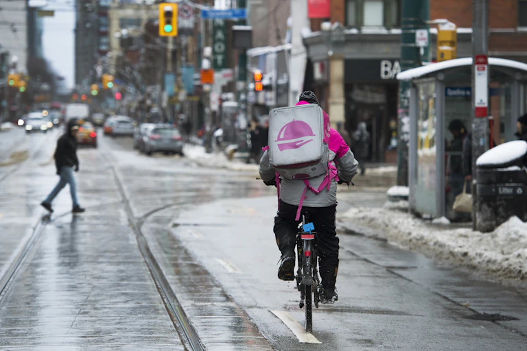 A Foodora courier rides their bike down a snow-lined street