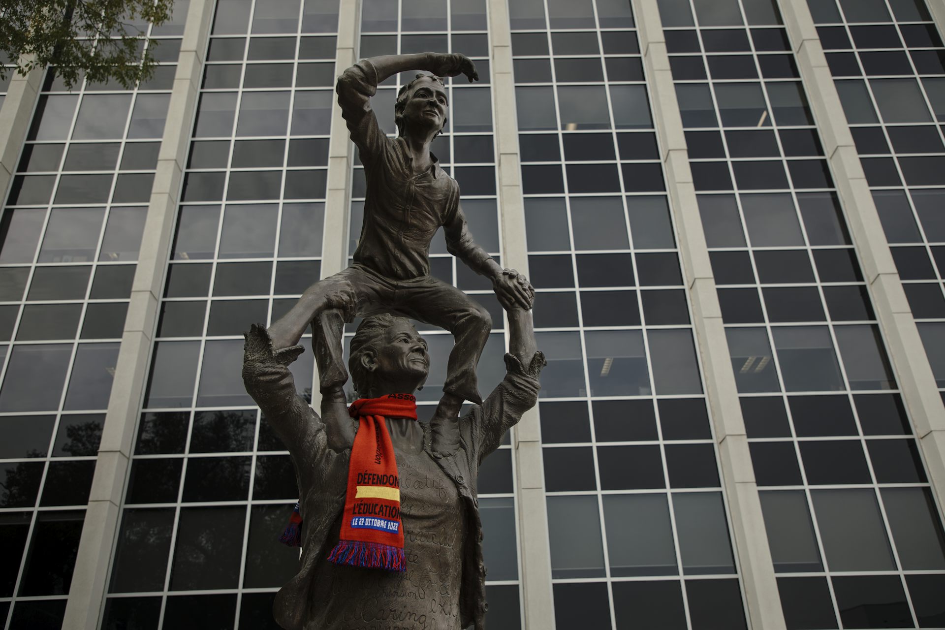 A statue of a child on an adult's shoulders and the adult is wearing a red scarf.