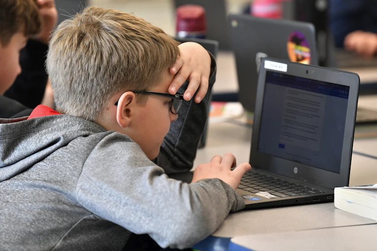 A boy at a laptop with his hand on his forehead.