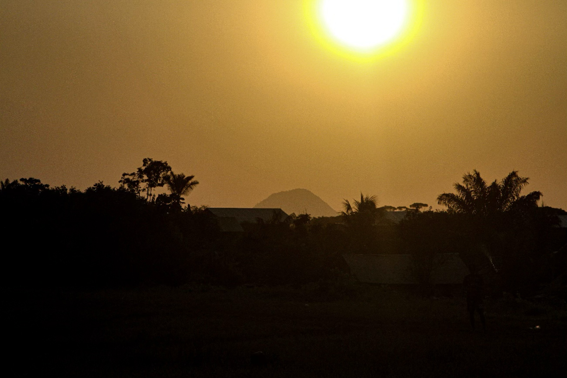 foto mostra aldeia contra a luz, com um sol forte no céu