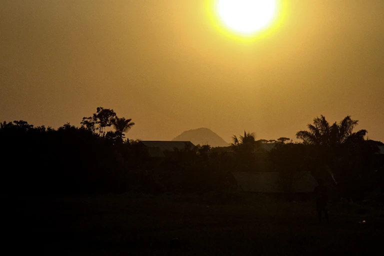 foto mostra aldeia contra a luz, com um sol forte no céu