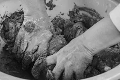 Foto em preto e branco mostra mãos amaçando a argila