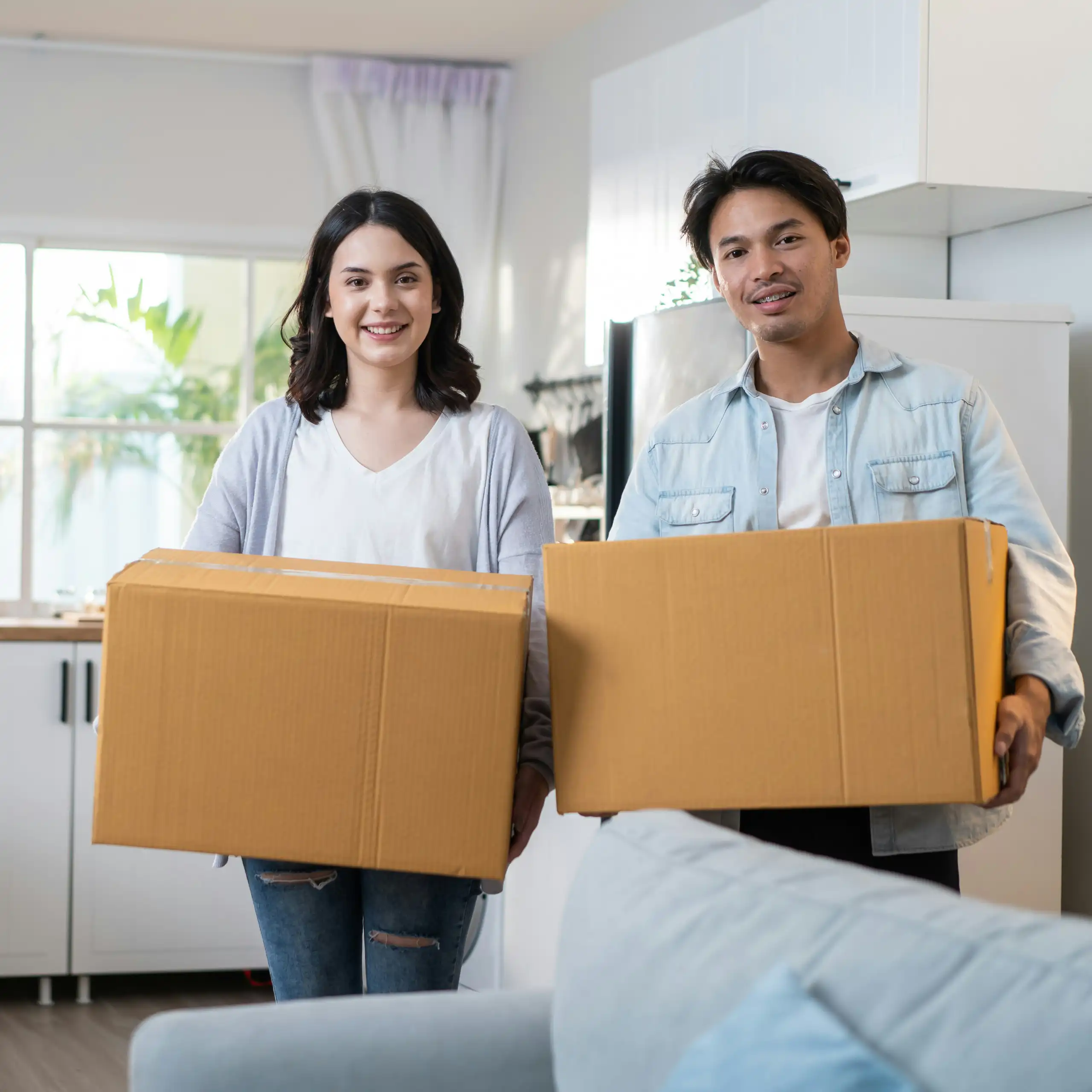 A man and a woman are standing in a the room of a house while holding moving boxes.
