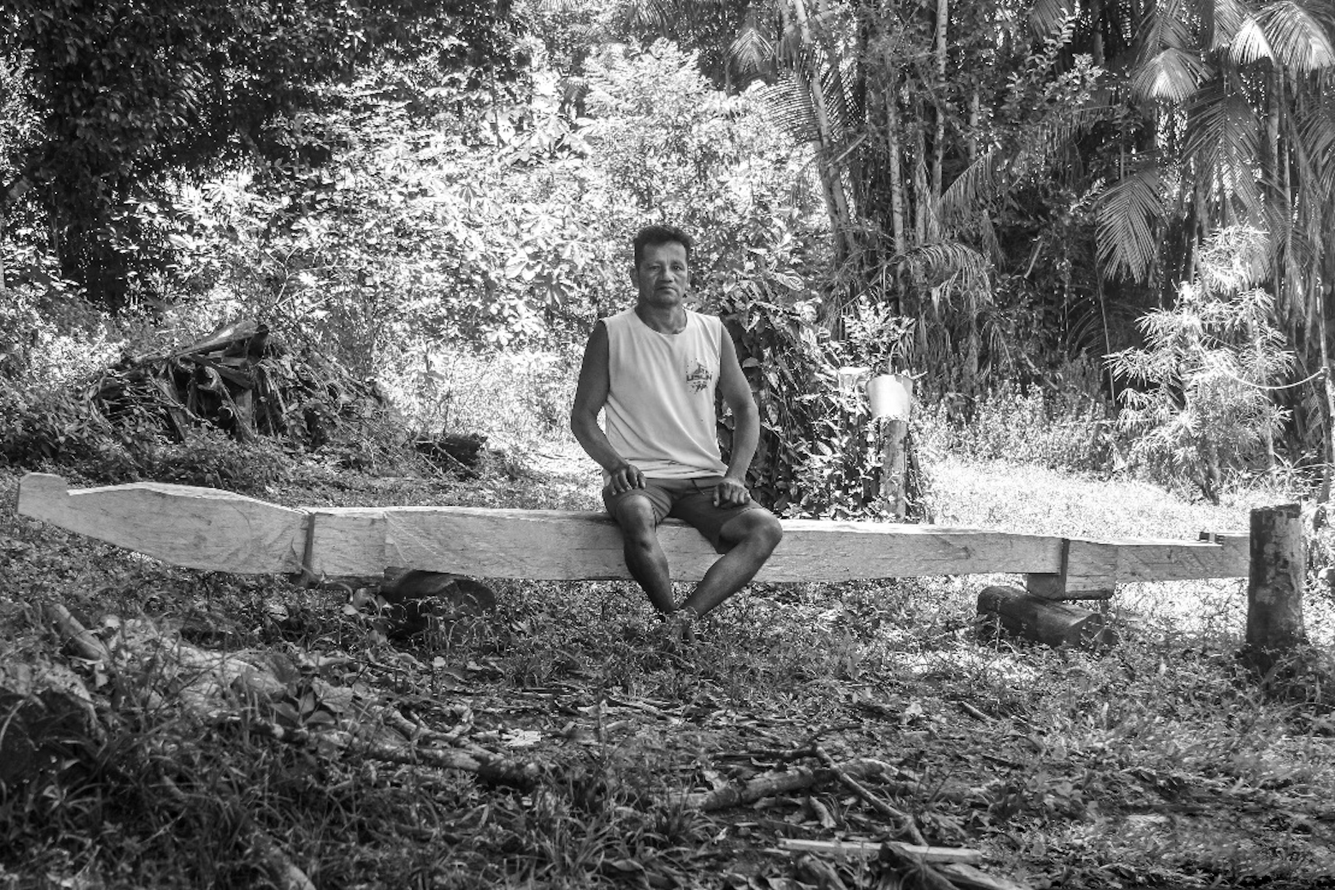 Foto em preto e branco mostra um homem sentado num banco, no meio do quintal