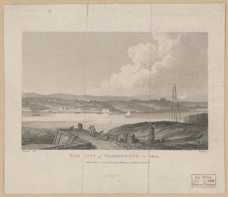 A view from across a river of a city, showing sparsely populated hills, an arched bridge, and some buildings along the waterfront with men and barrels in the foreground.