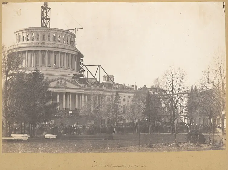 A crowd attending ceremony with construction on dome of U.S. Capitol in background.