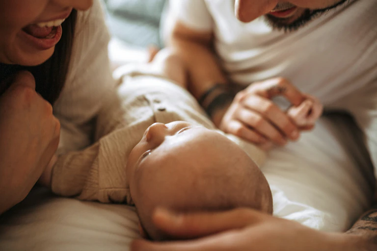 A baby laying down looking up at a woman and a man