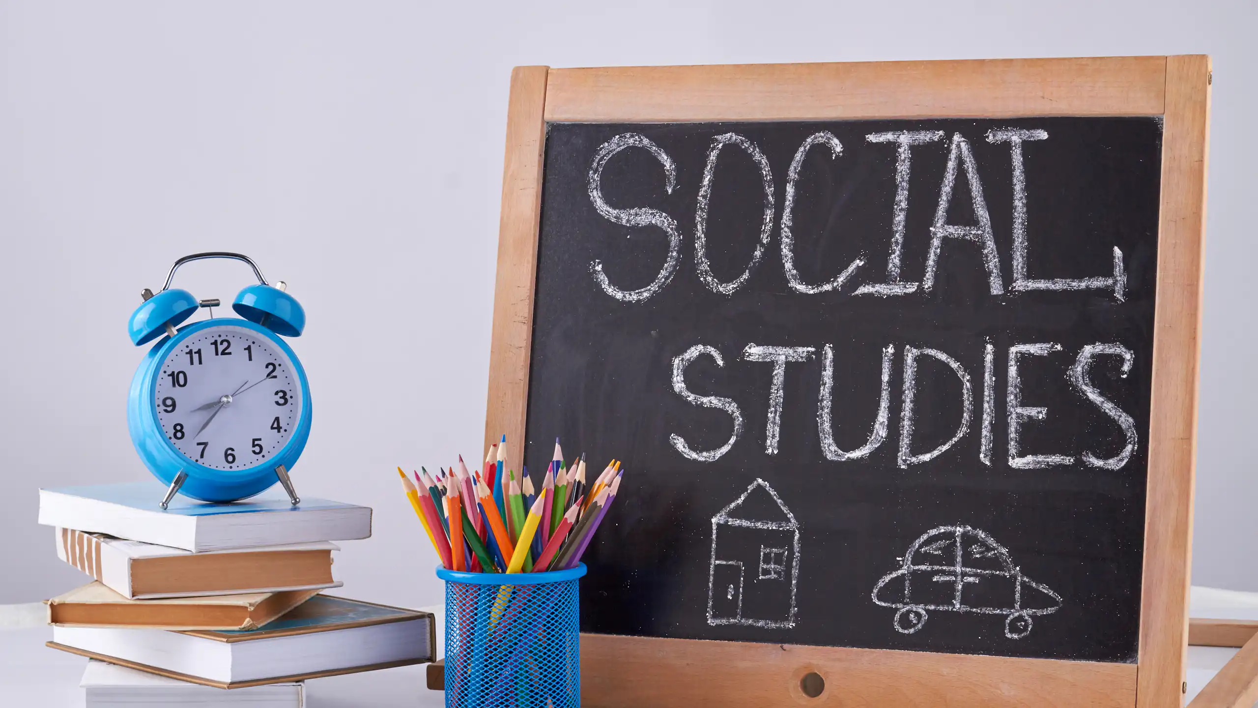Despertador, vaso con lápices y una pizarra donde puede leerse "Social studies".