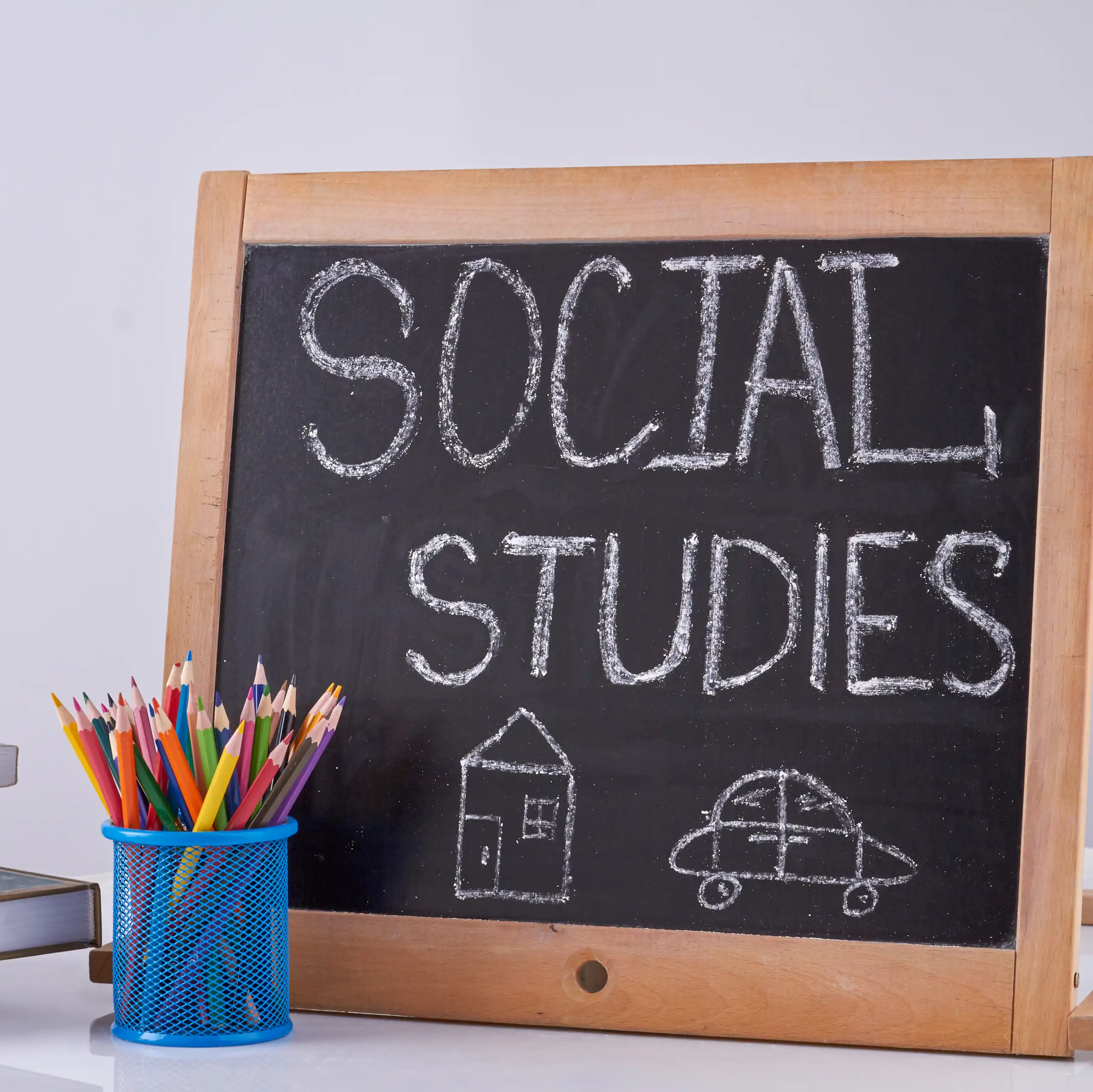 Despertador, vaso con lápices y una pizarra donde puede leerse "Social studies".
