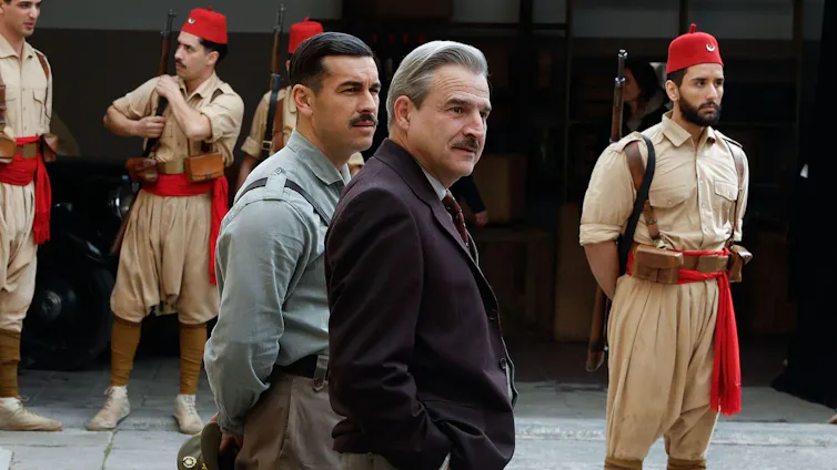 Dos hombres pasean entre soldados de uniforme del norte de África.