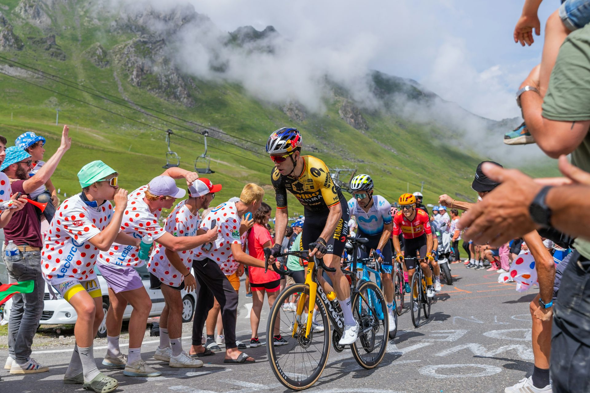 Uns ciclistes en una competició amb muntanyes de fons i aficionats al costat de la carretera.