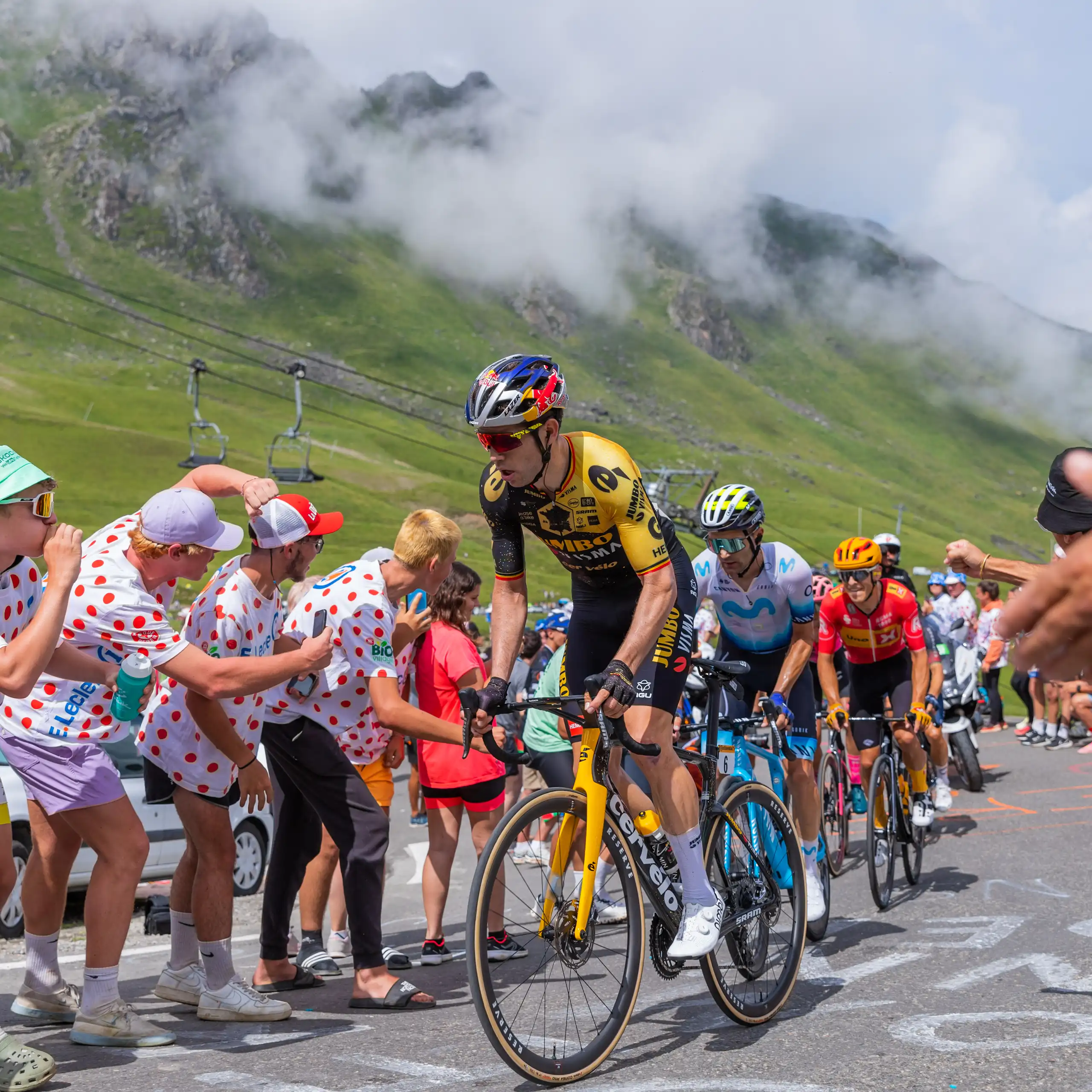Uns ciclistes en una competició amb muntanyes de fons i aficionats al costat de la carretera.