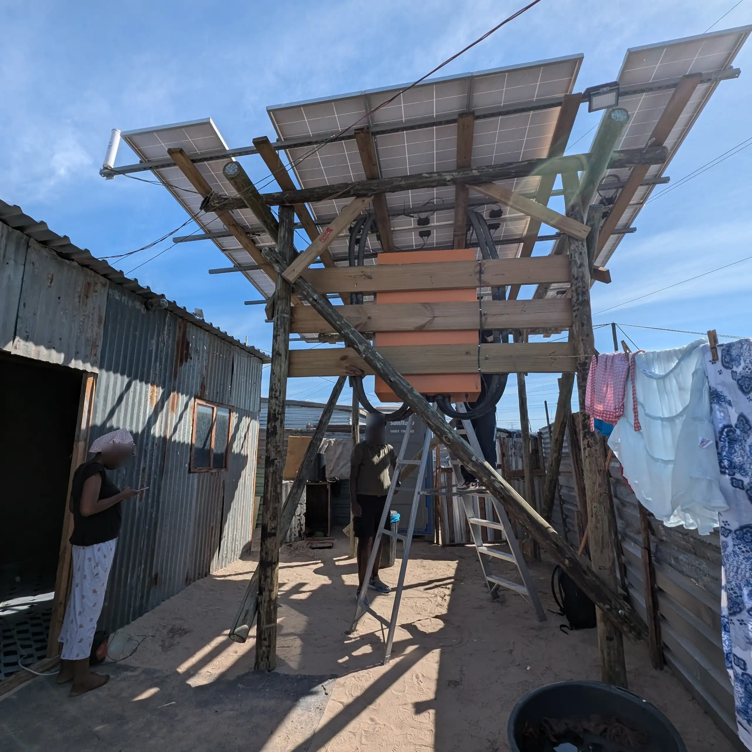A shack made of corrugated metal with three solar panels mounted on poles outside, generating energy for the residents.