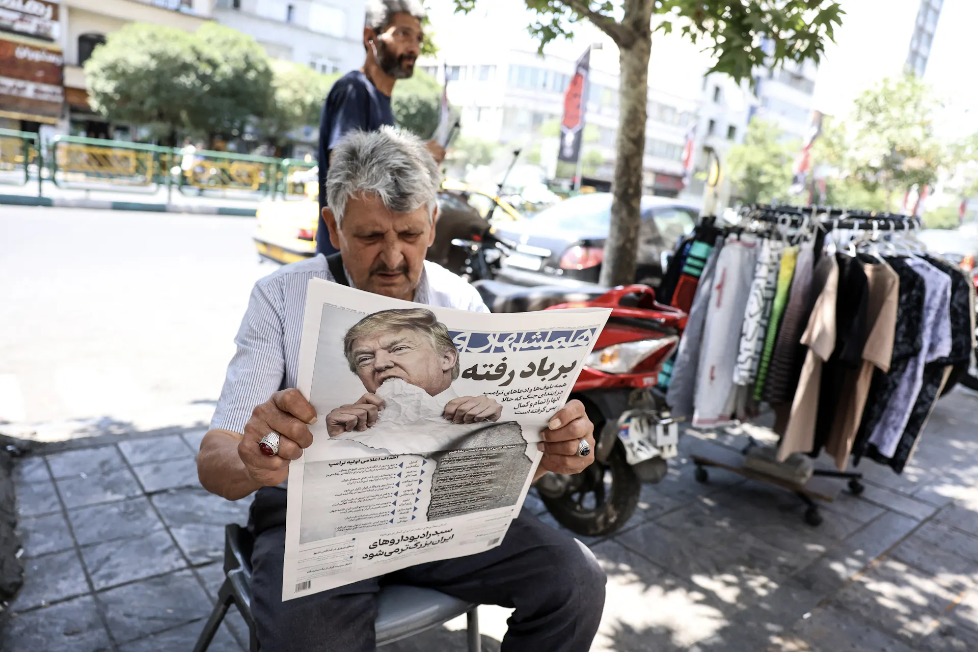 A man sitting outdoors reads a newspaper.