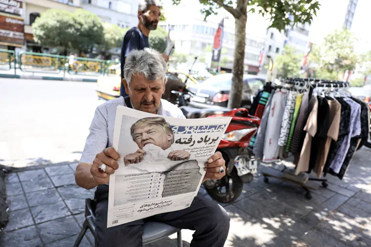 A man sitting outdoors reads a newspaper.