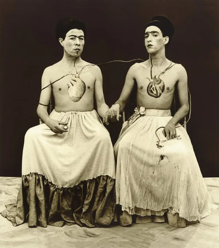 Recreation of a Kahlo painting, two people sat hand in hand.